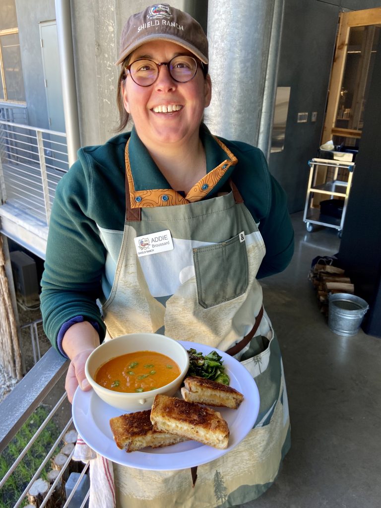 Chef Addie holding a plate with soup, salad, and grilled cheese sandwiches. 